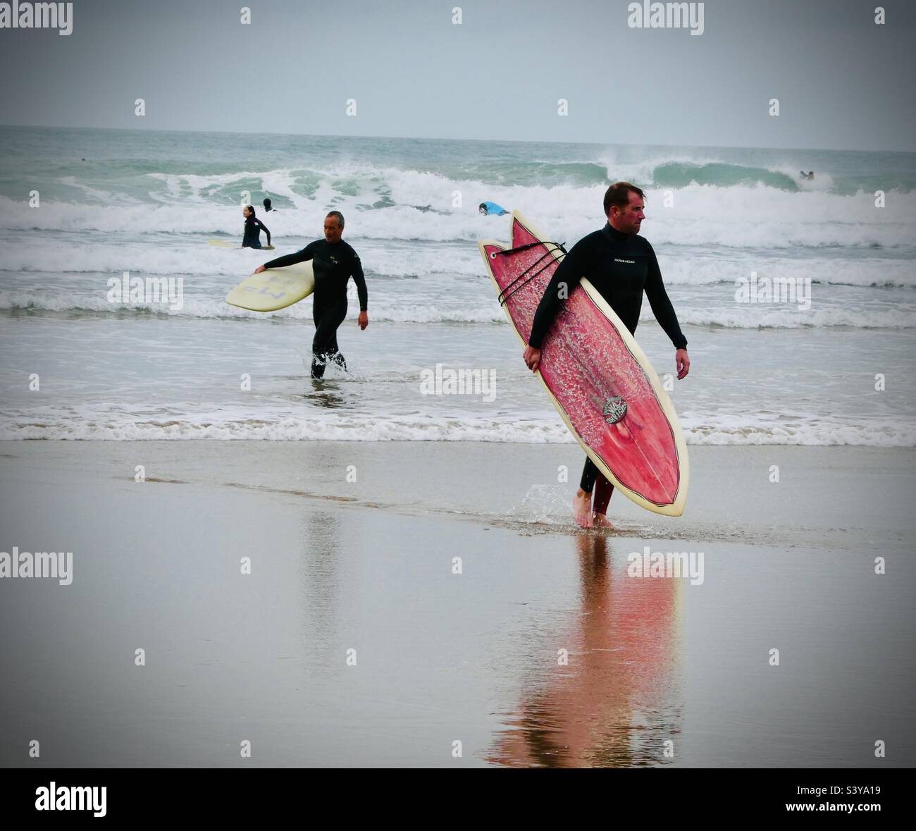 Two surfers come from the sea carrying their surfboards at Saunton Sands in North Devon in