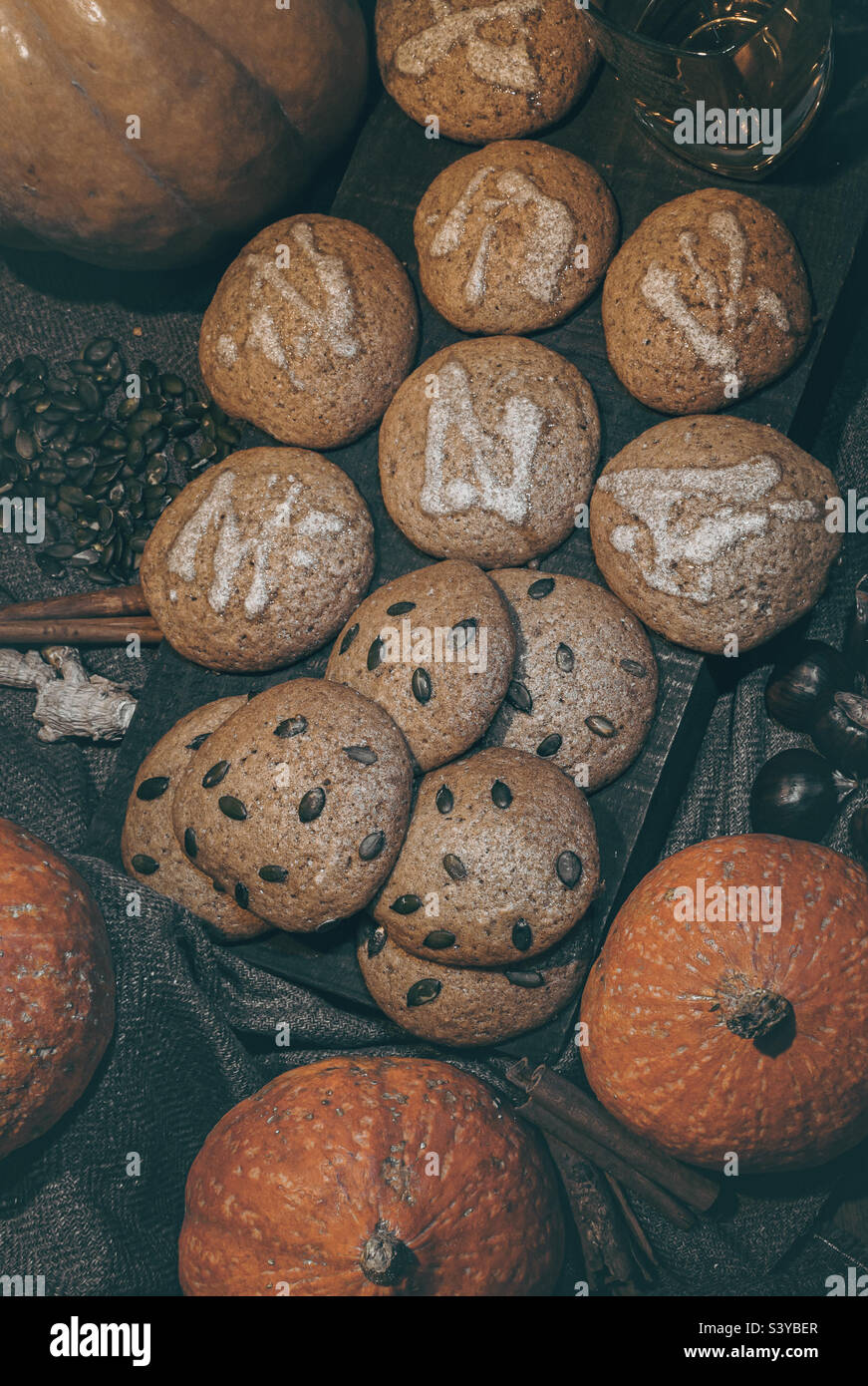 A wood platter of iced and seeded pumpkin cookies, surrounded by autumnal ingredients - Smartphone Captured Stock Image