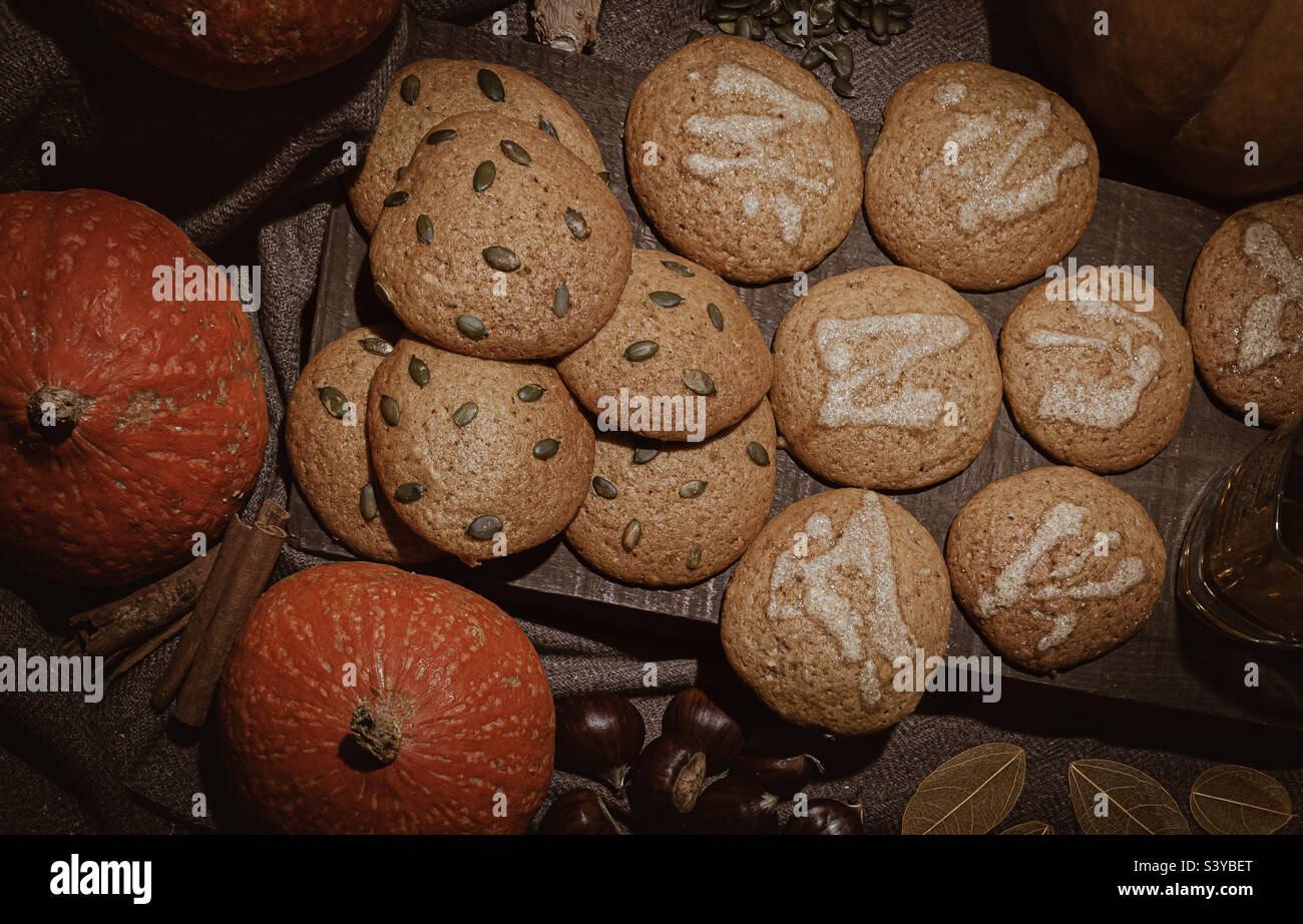 A wood platter of iced and seeded pumpkin cookies, surrounded by autumnal ingredients - Smartphone Captured Stock Image