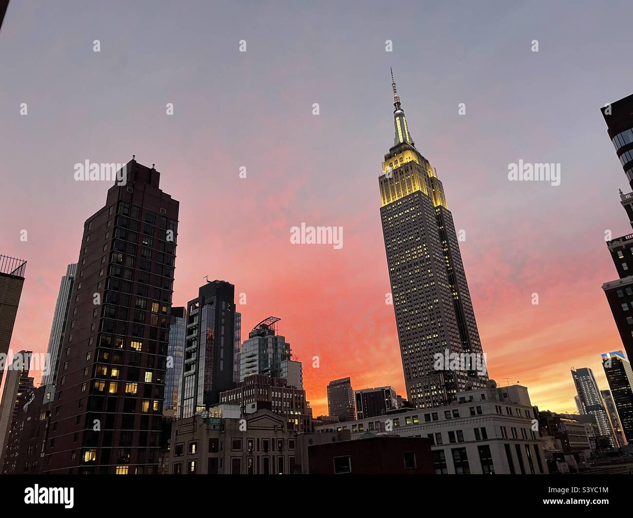 The Empire State building is silhouetted against a brilliant red sky at dusk in New York City, USA - Smartphone Captured Stock Image