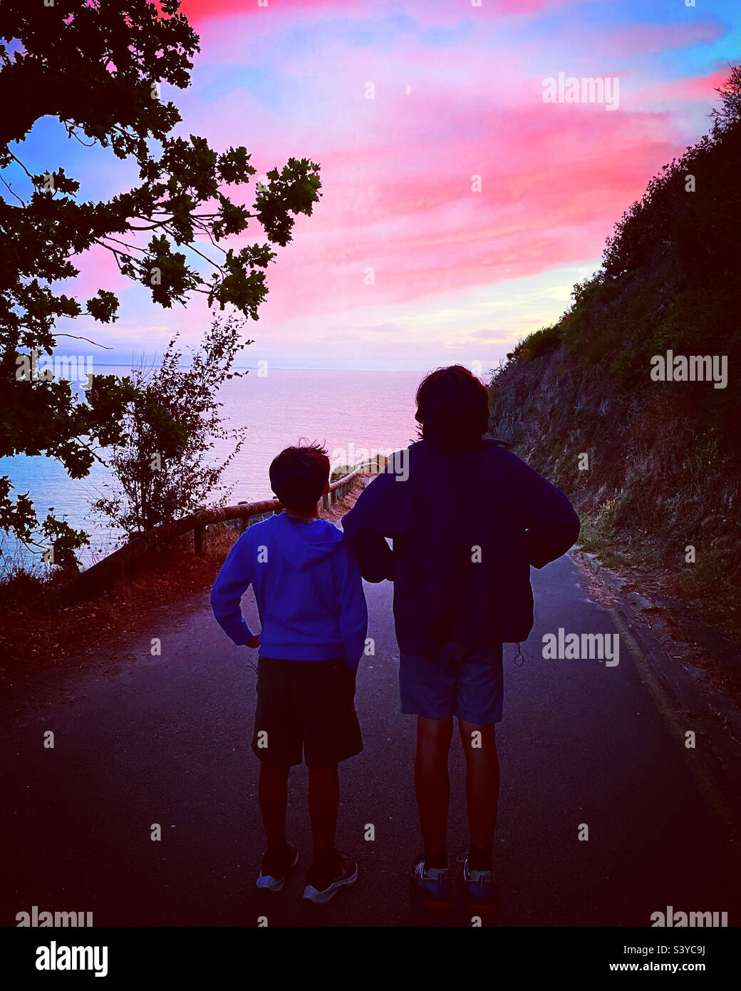 2 friends looking at a pink sunset on the ocean - Smartphone Captured Stock Image
