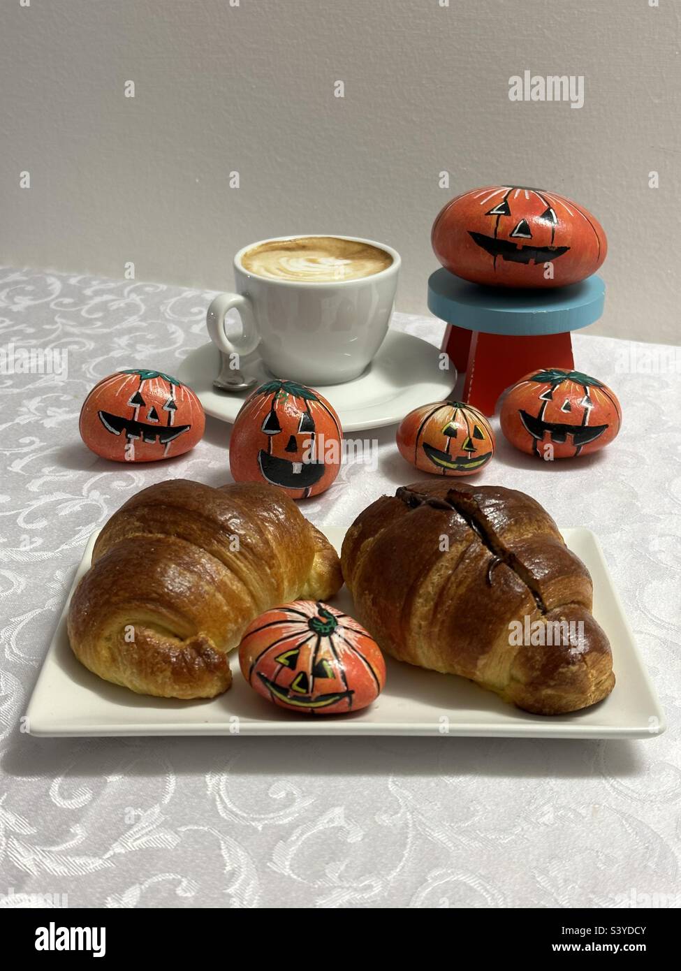 Halloween breakfast with cappuccino, croissants and stone hand painted pumpkins at the bar Stock Photo