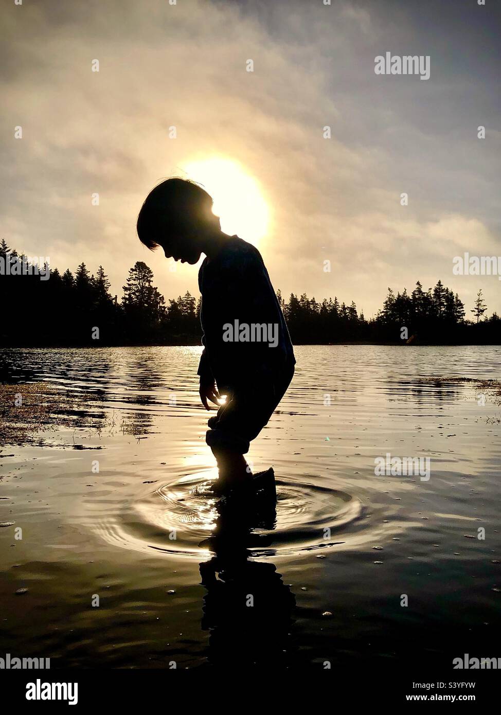 Kid in a cove of the Atlantic Ocean at sundown. Shallows. Steps create a puddle. Getting feet wet, literally. Age-old, simple fun. Time honoured. Outdoors. - Smartphone Captured Stock Image