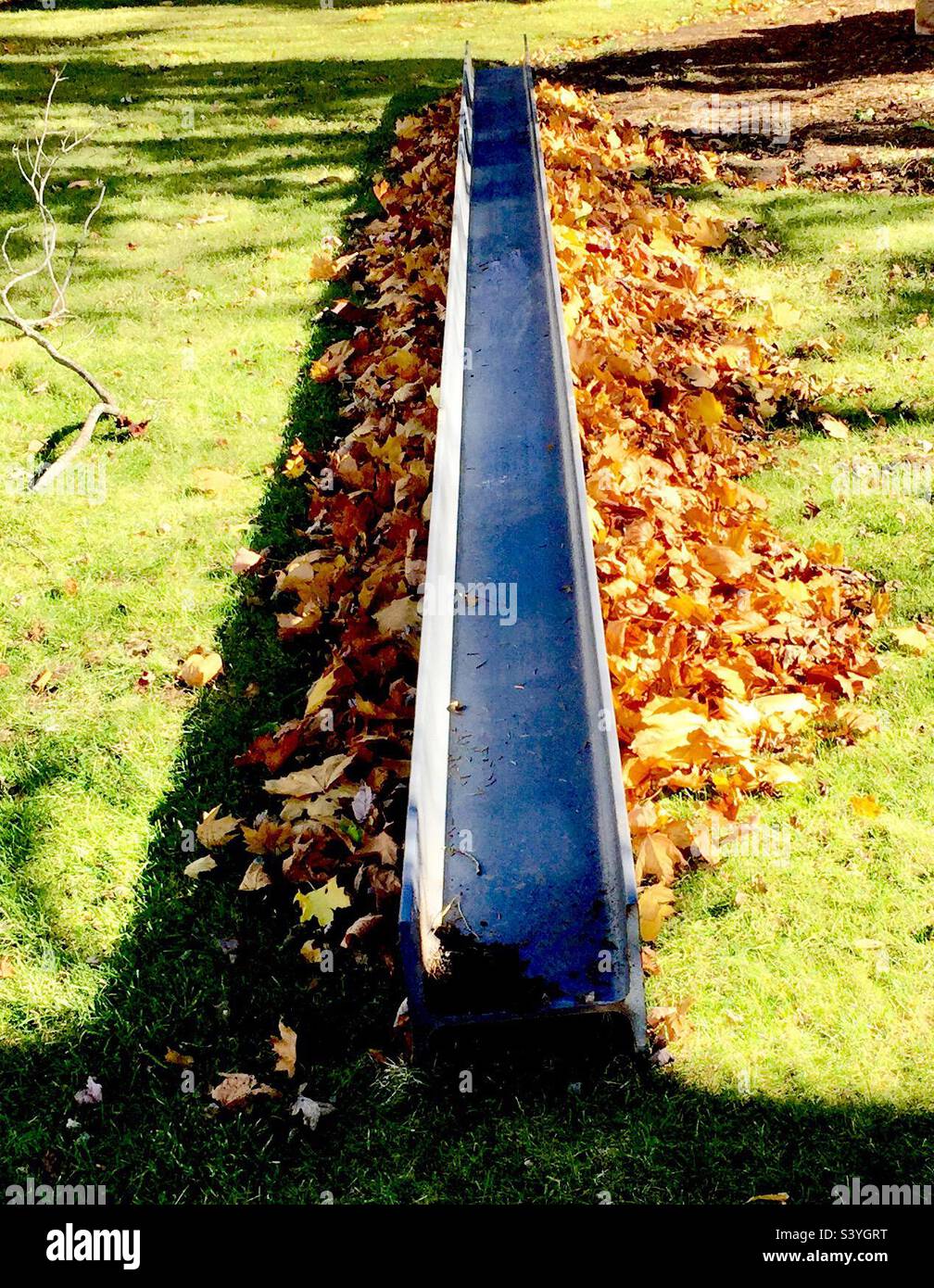 Steel beam and fallen leaves lying on the ground. Nature soft, man made object hard. Juxtaposition. Hard soft. Stock Photo