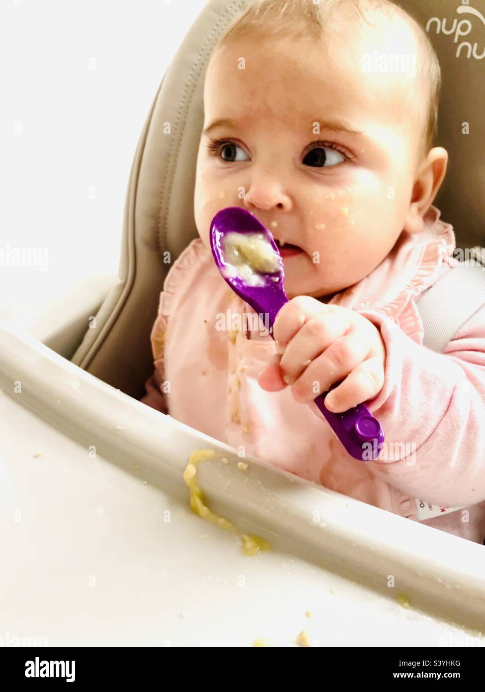 Baby girl weaning, feeding herself with purple spoon Stock Photo