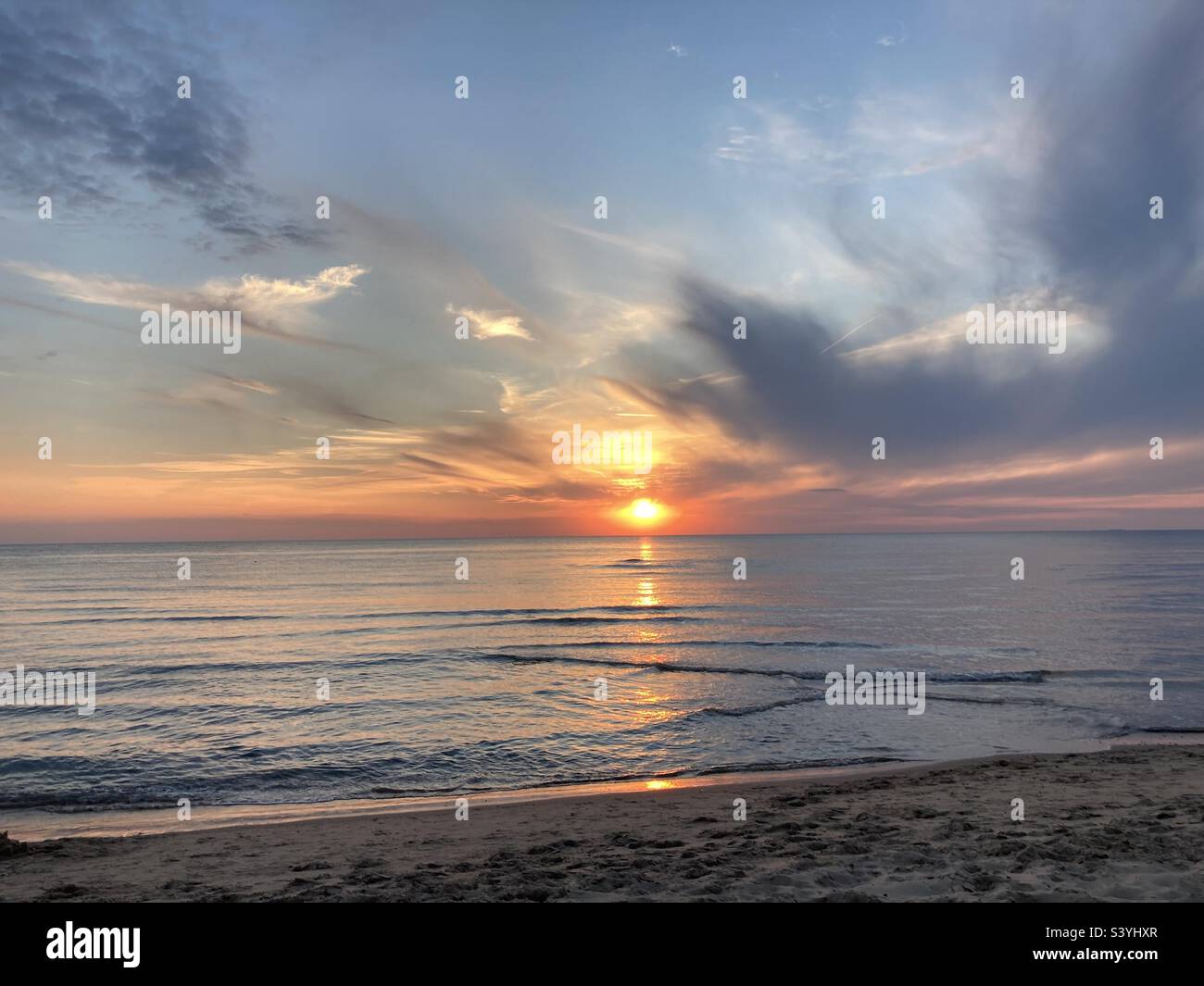 at the sea the red-golden sun shines out from behind the clouds before it sets - Smartphone Captured Stock Image