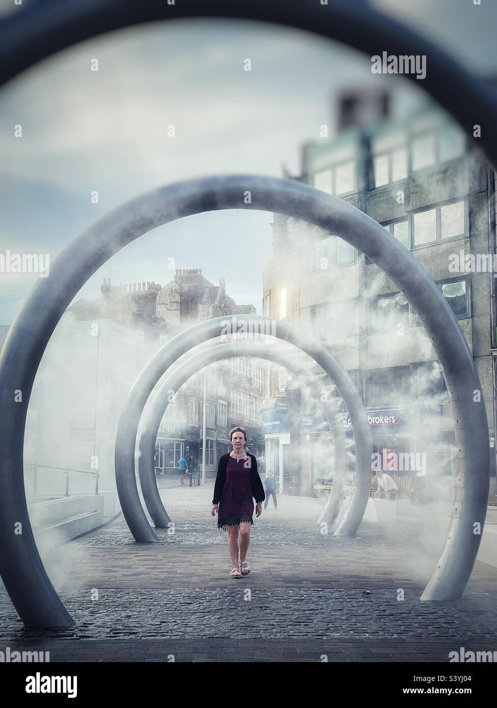 Woman walking through steaming metal ring street art installation in Dover town, England. Stock Photo