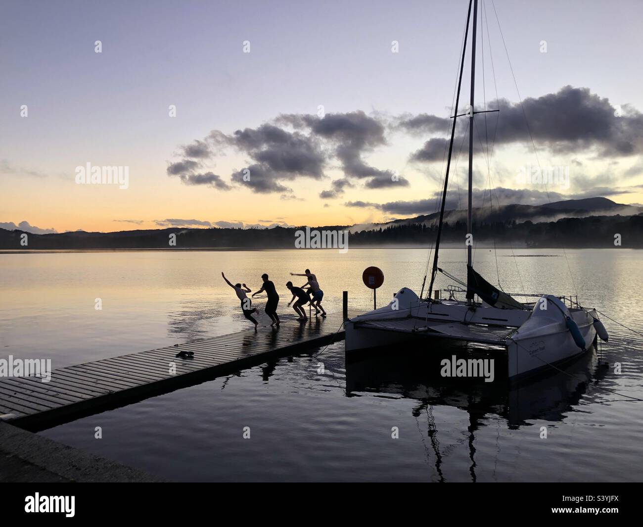 Wild swimming jumping from the jetty for fun into Lake Windermere at dusk, Cumbria Lake District - Smartphone Captured Stock Image