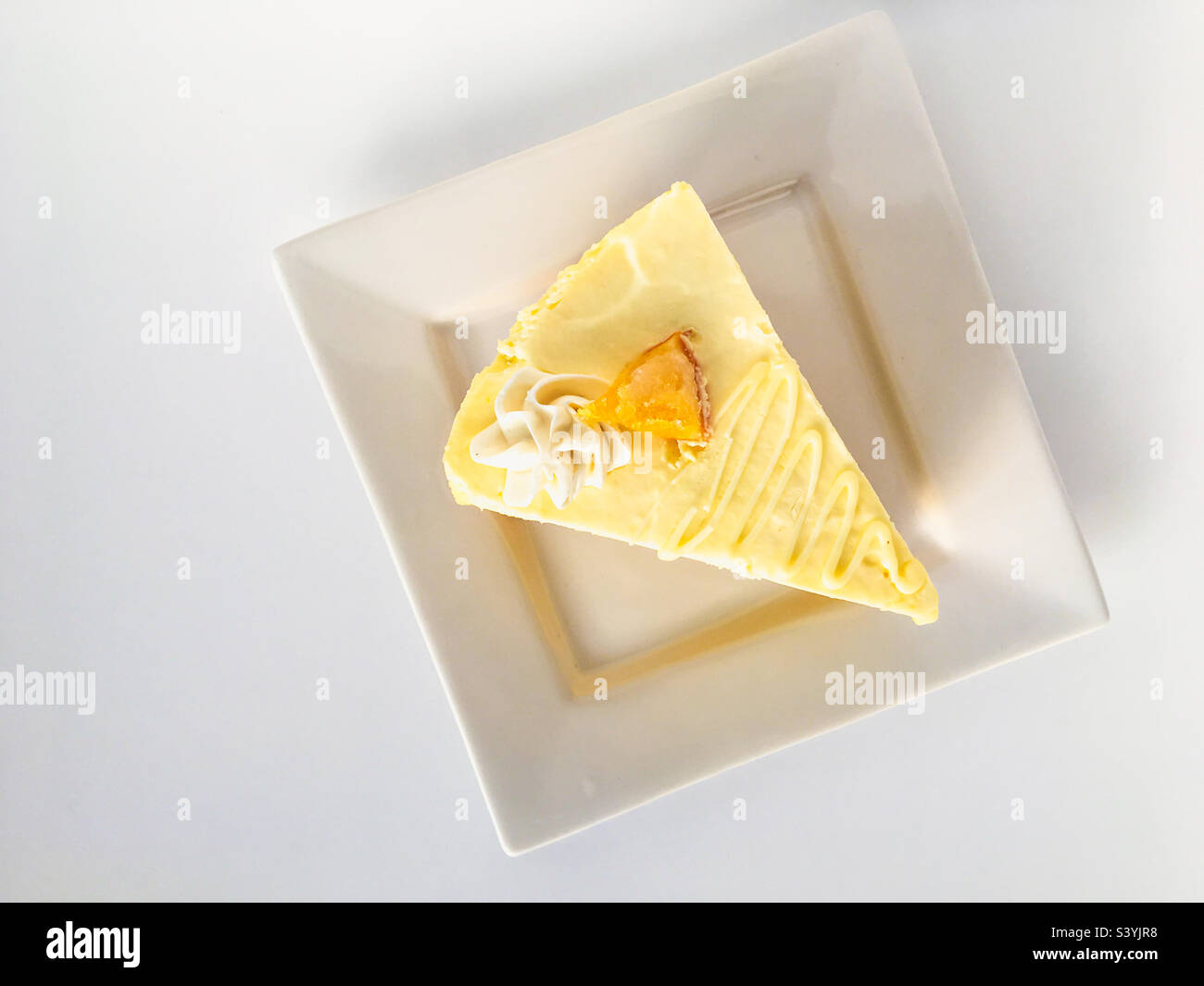 High angle view of a slice of fresh fruity mousse cake on a square white plate on white background. Stock Photo