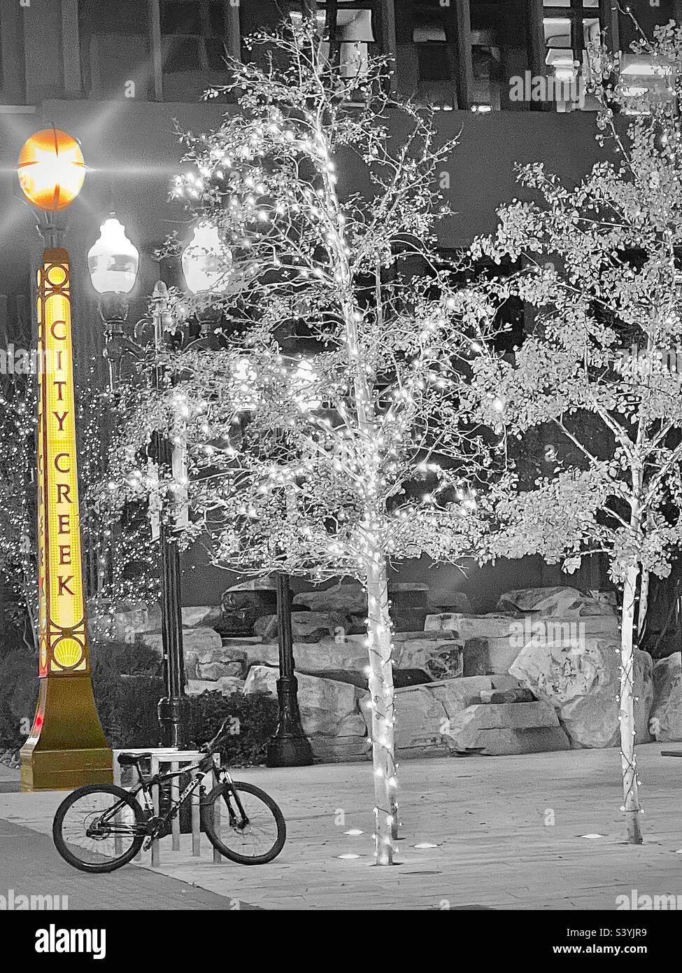 In downtown Salt Lake City, Utah, USA at the City Creek Center shopping complex during the Christmas season. The Christmas lights sparkle, even in B&W. A lone bike stands under the glowing lamppost. - Smartphone Captured Stock Image