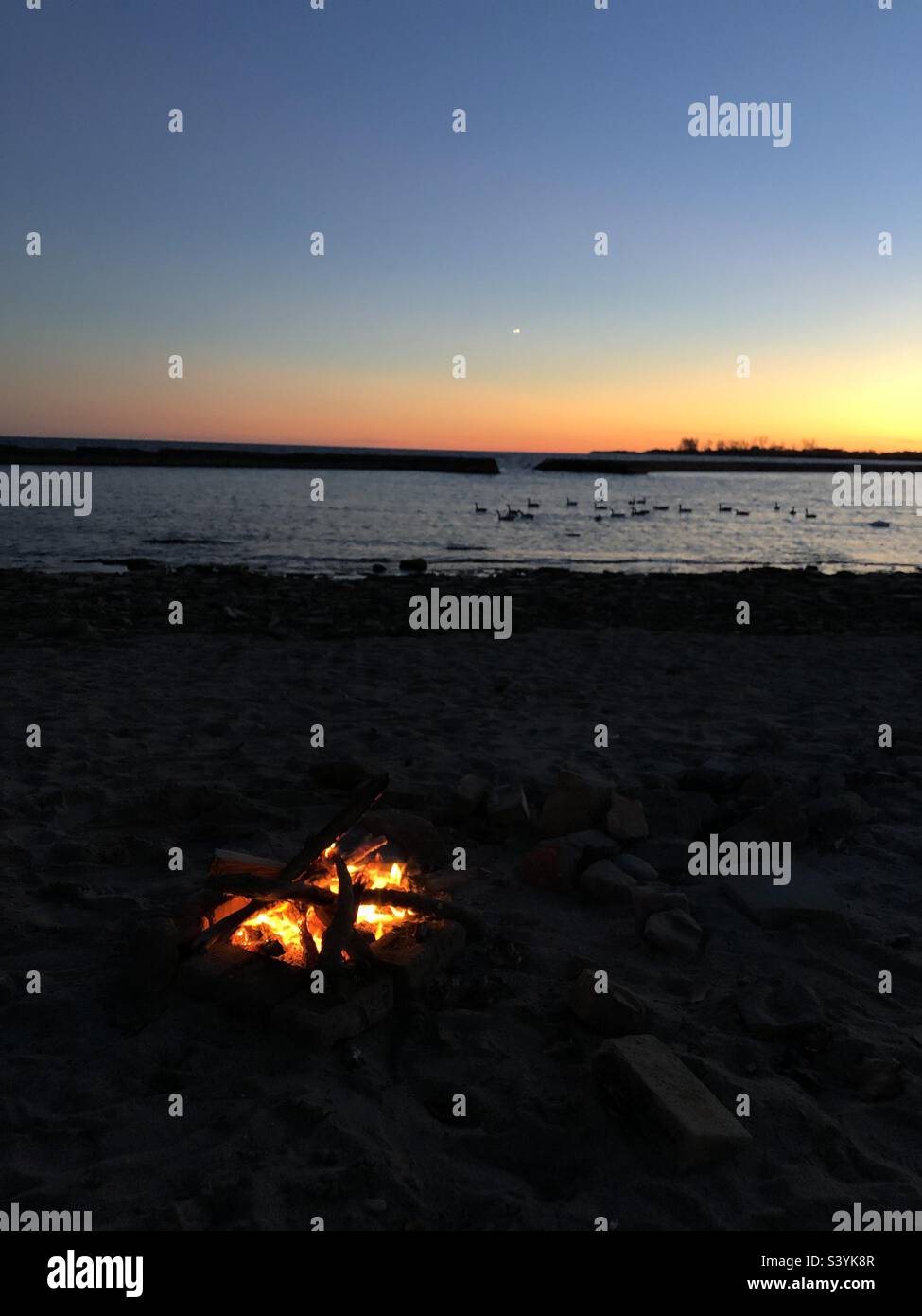 Campfire on the beach as the sun sets. - Smartphone Captured Stock Image