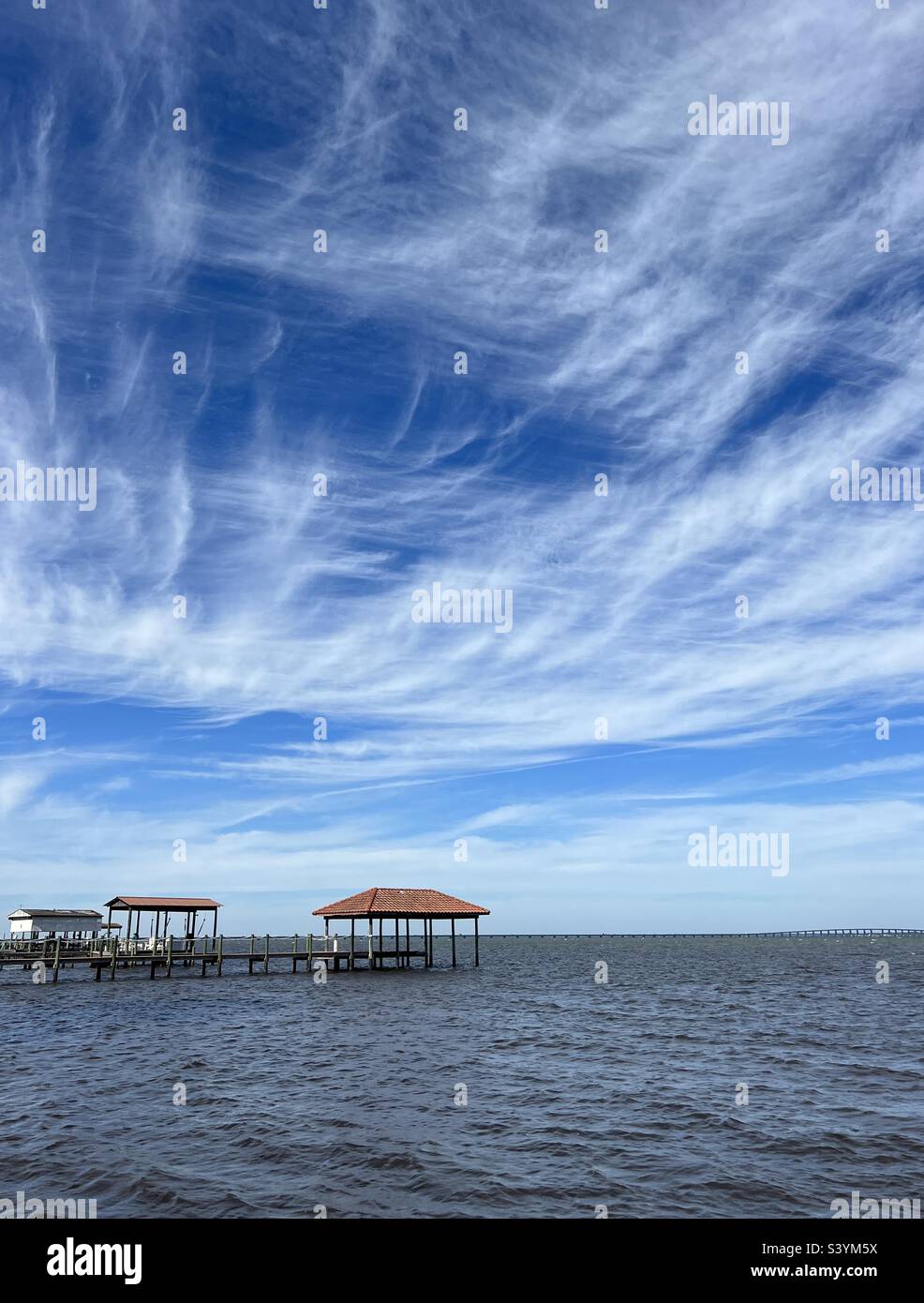 Feathery white clouds with deep blue skies over bay water Stock Photo ...