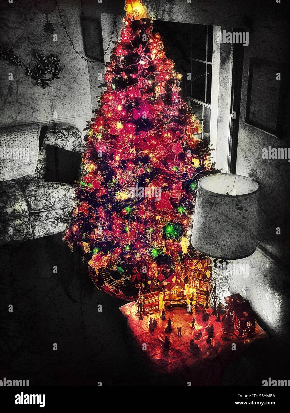 A darkened living room in a home in Utah, USA filled only with the glowing amber light of the lighted Christmas tree and other holiday decorations. Grunge digitally added for a more vintage look. - Smartphone Captured Stock Image