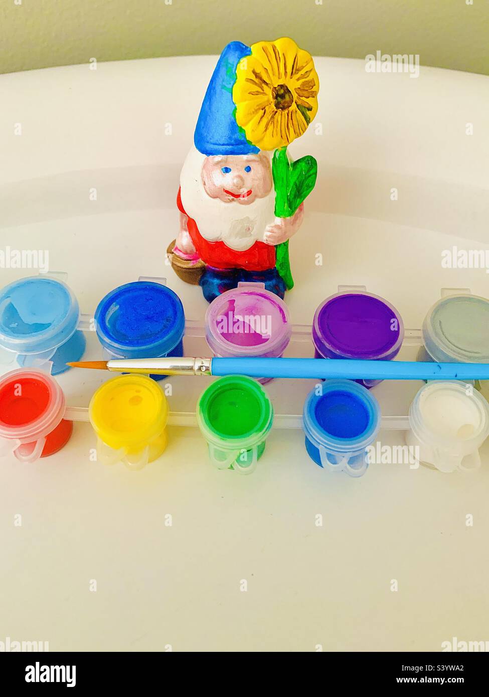 Colorful freshly hand painted gnome stands against white background behind paint set and paintbrush - Smartphone Captured Stock Image