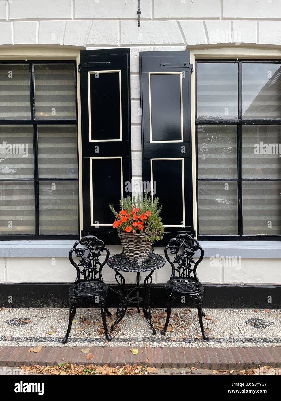 Table and chairs with red flowers outside a shuttered building in Elburg, Netherlands. - Smartphone Captured Stock Image