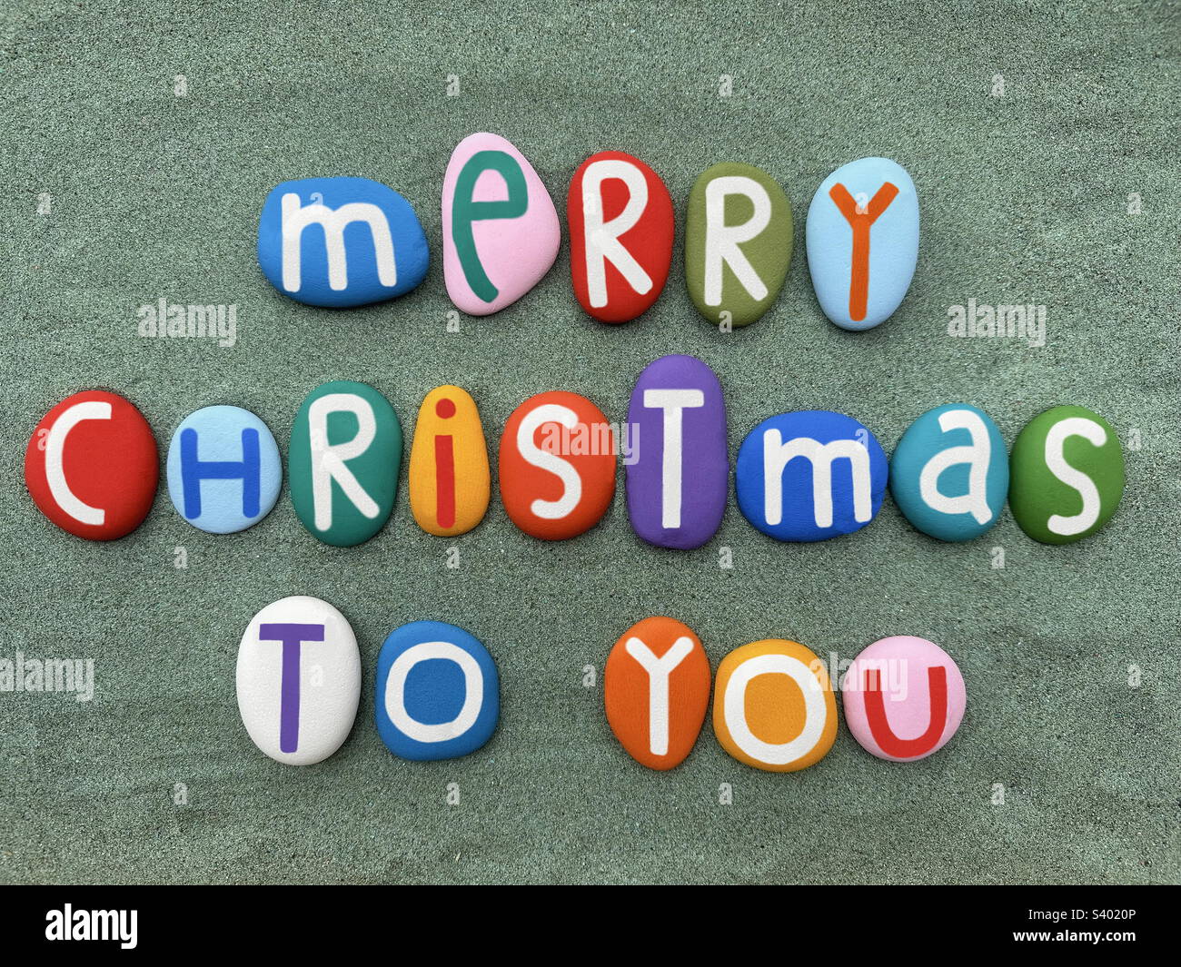 Multi colored Merry Christmas composed with hand painted stone letters over green sand - Smartphone Captured Stock Image