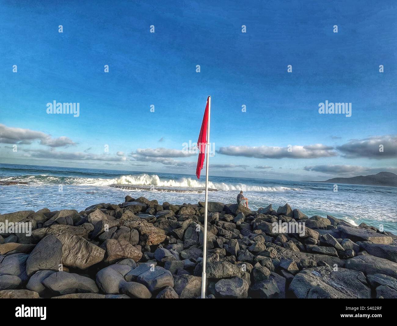 Red flag flies over the rocks looking out to the Atlantic Ocean - Smartphone Captured Stock Image