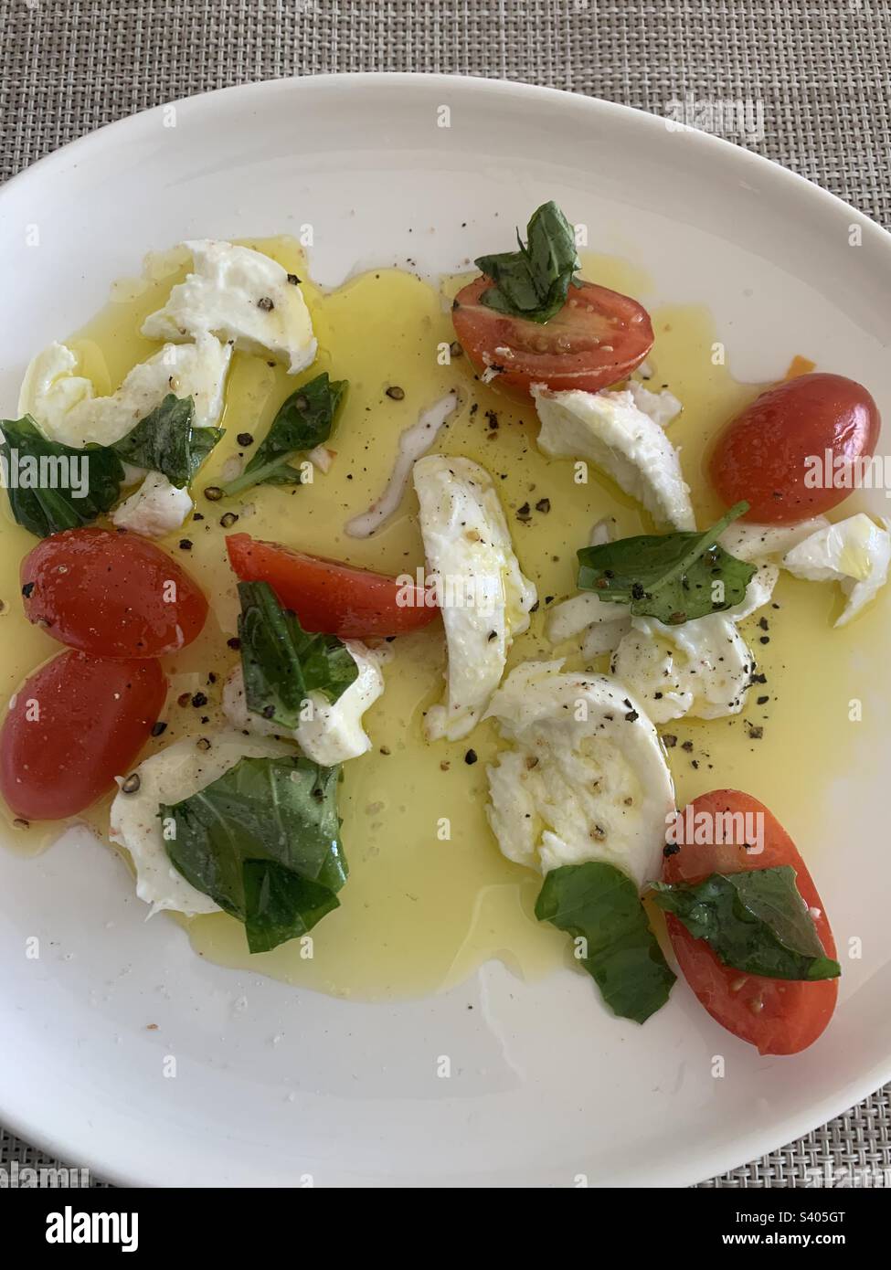 Close up image of a tomato and mozzarella salad topped with fresh basil leaves and drizzled with extra virgin olive oil - Smartphone Captured Stock Image