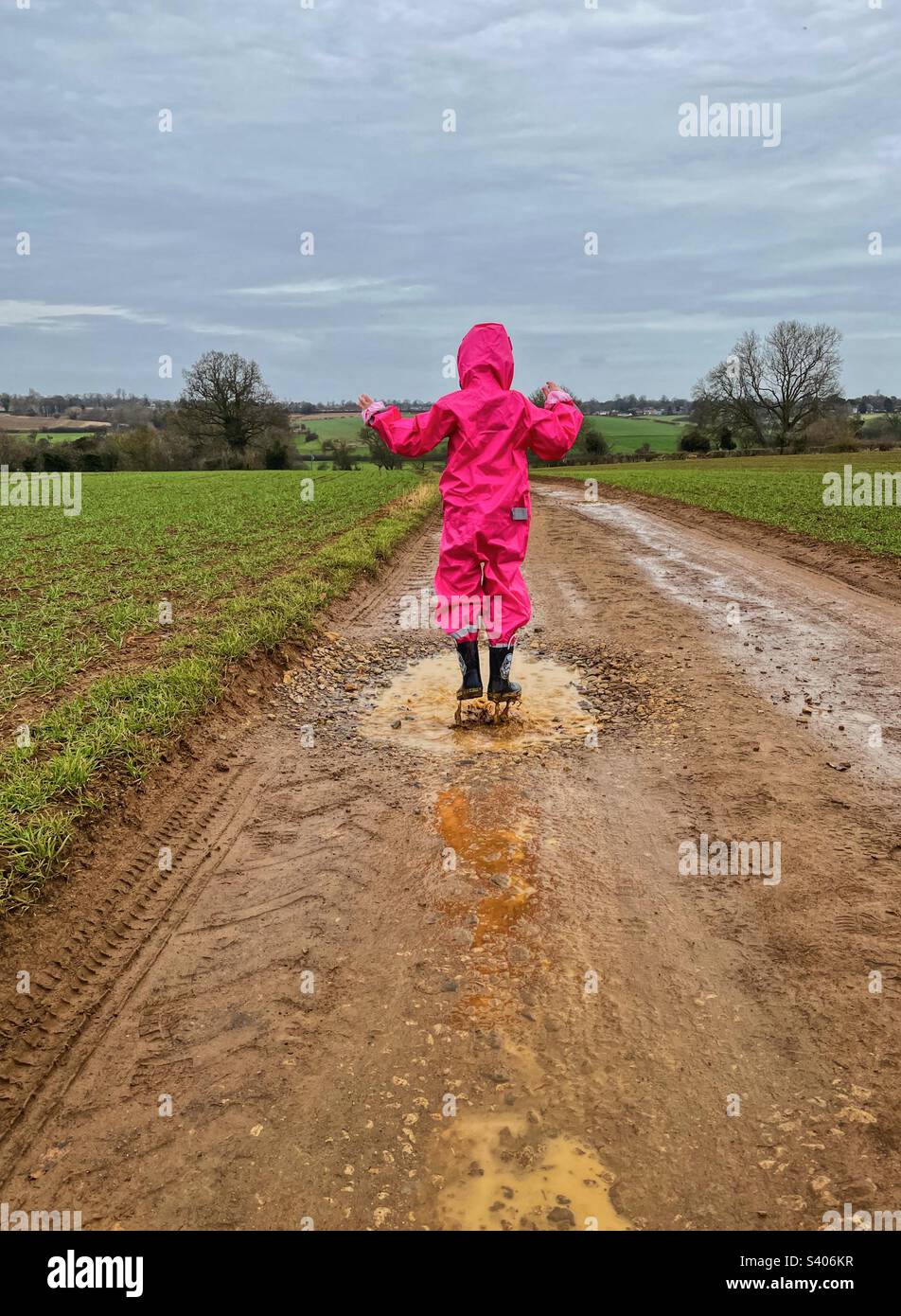 Rear view of girl jumping in muddy puddle on rural road in the rain. - Smartphone Captured Stock Image
