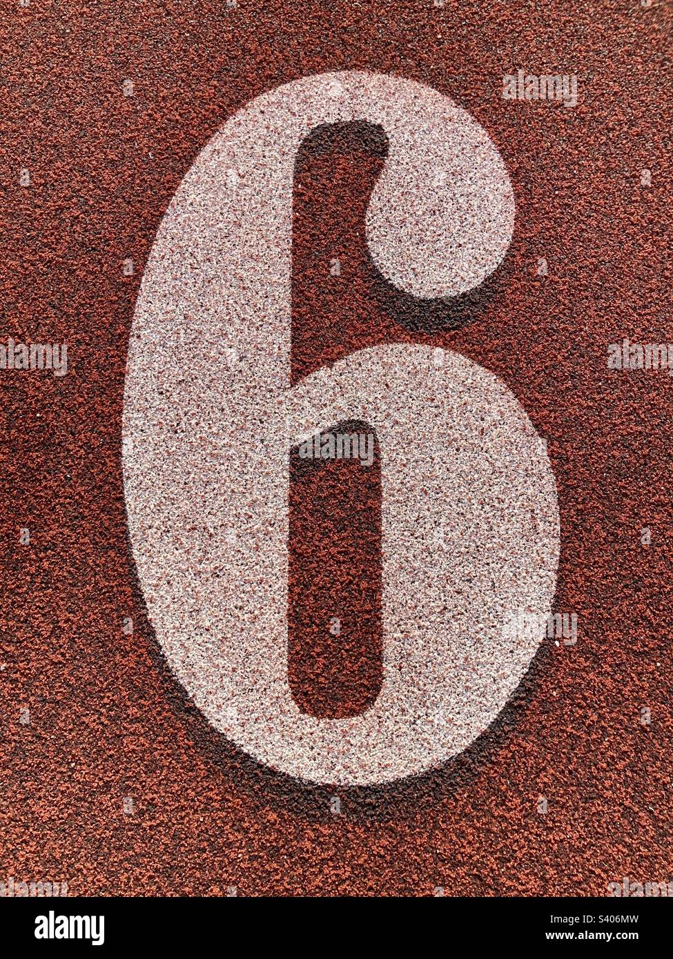 The number six (6) on track and field turf. White lettering with red, textured background. Stock Photo