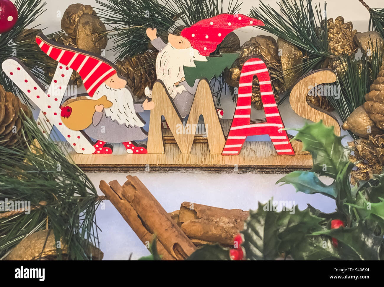 Wooden sign of the word Xmas surrounded by a pine cone garland