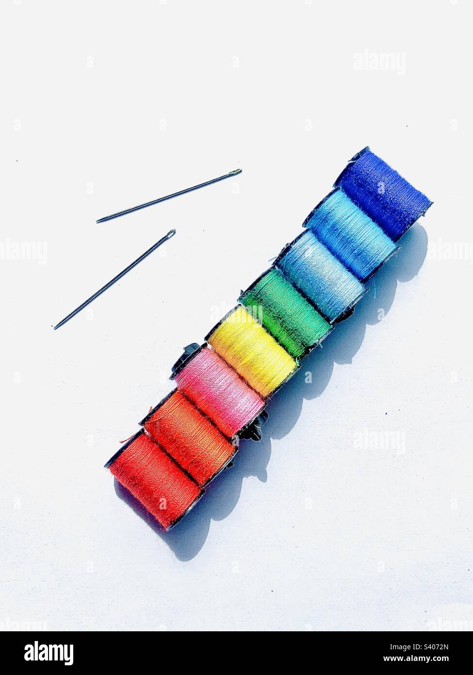 Rainbow colored thread and 2 sewing needles against stark white background with copy space - Smartphone Captured Stock Image