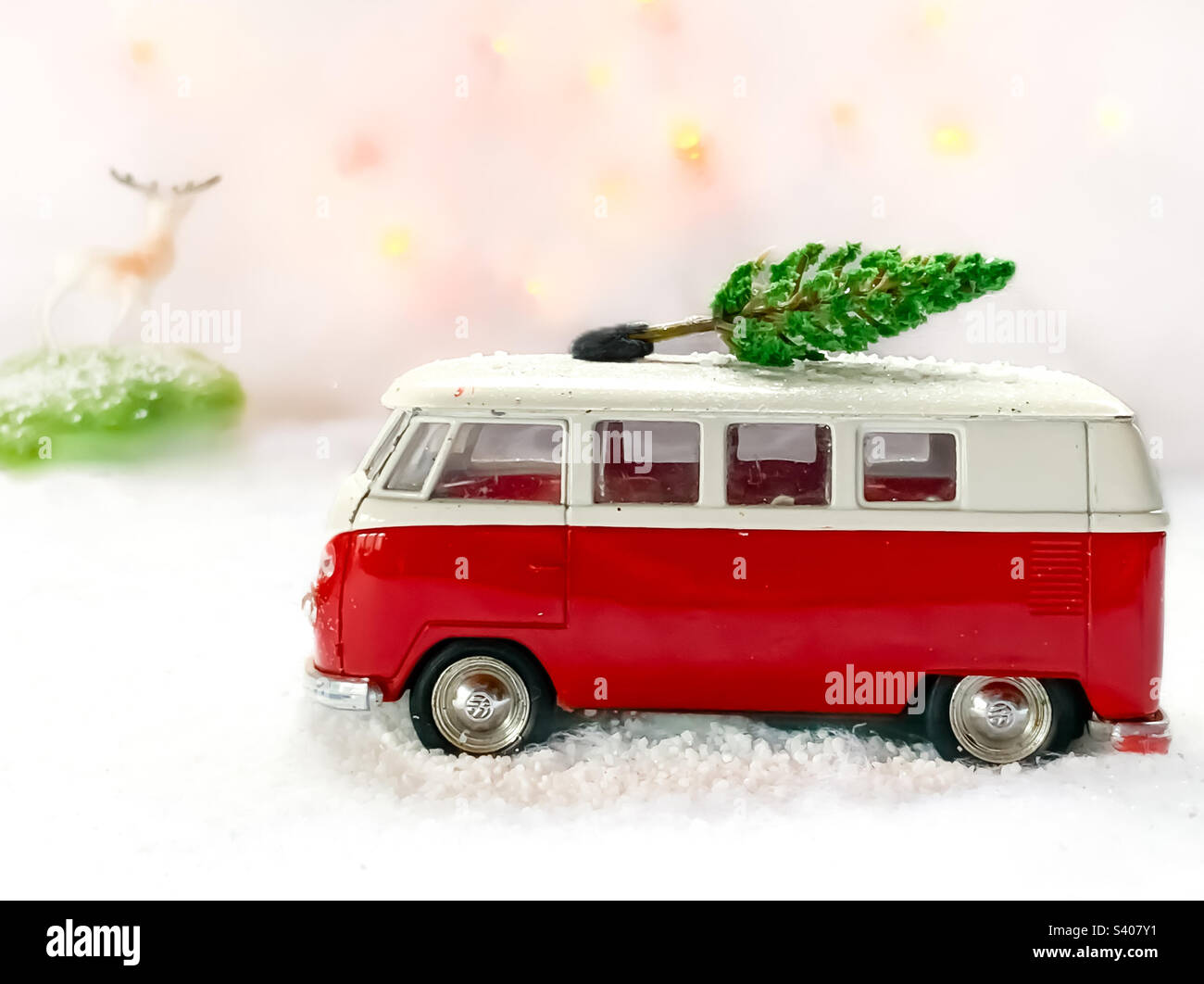 Red toy camper drives through a snowy scene with a Christmas tree on its roof, watched by a toy deer on a hill in the distance. - Smartphone Captured Stock Image