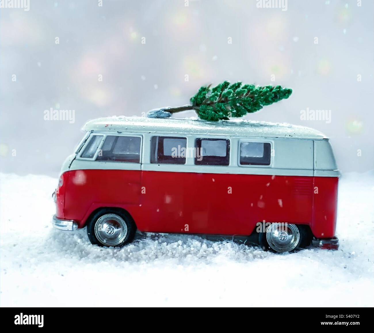 Red toy camper drives through a snowy scene with a Christmas tree on its roof - Smartphone Captured Stock Image