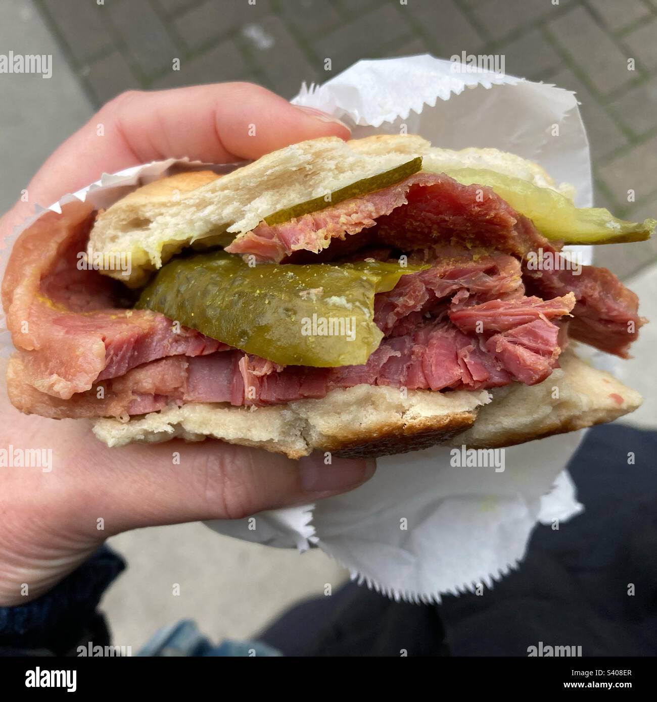 Hot salt beef bagel with gherkin in a woman’s hand - Smartphone Captured Stock Image