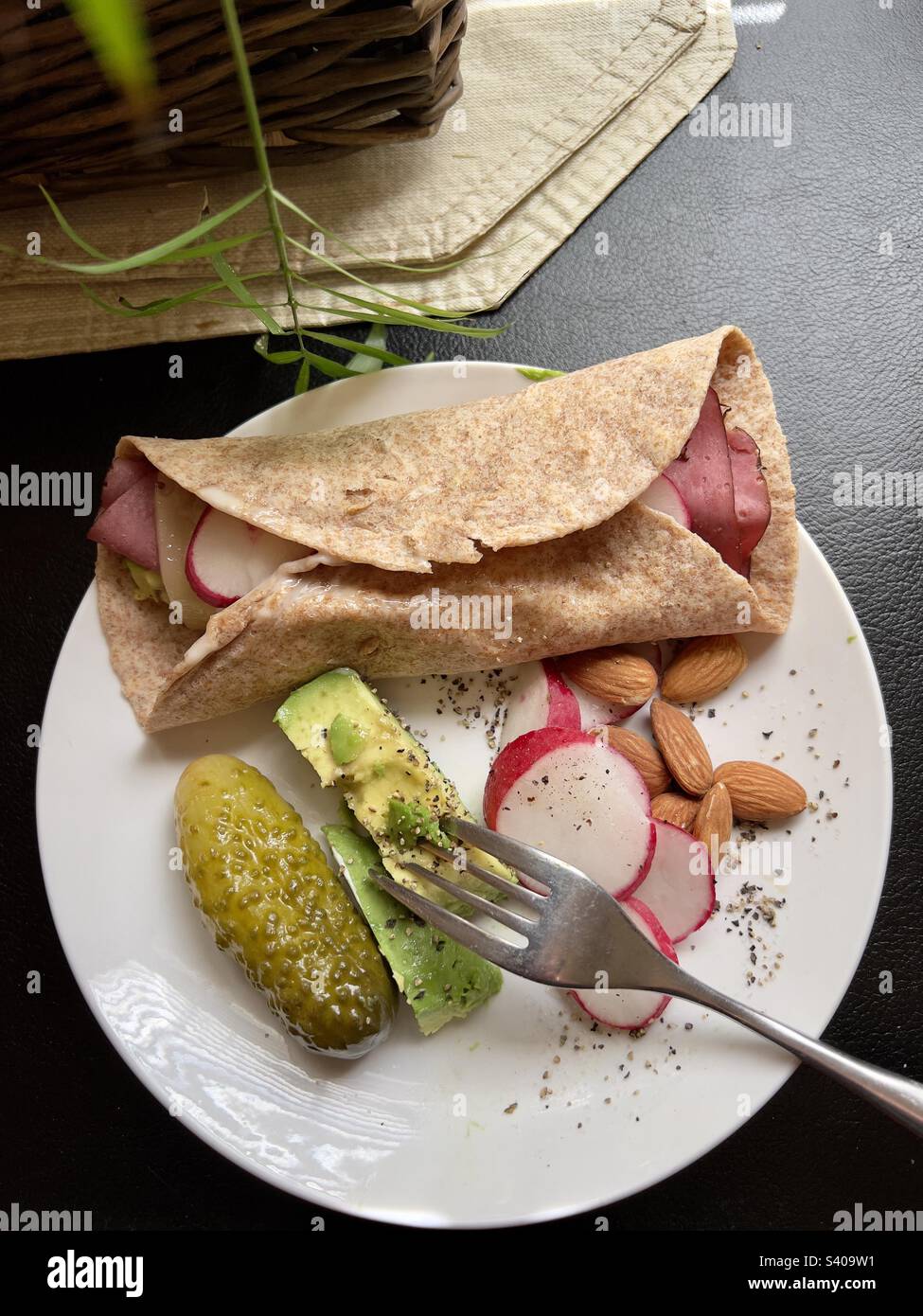 Eating healthier with the Mediterranean diet. Wheat tortilla wrap with lunch meat, avocados, and Swiss cheese. Served with h almonds, radish, pickle and a slice of fresh avocado. Stock Photo