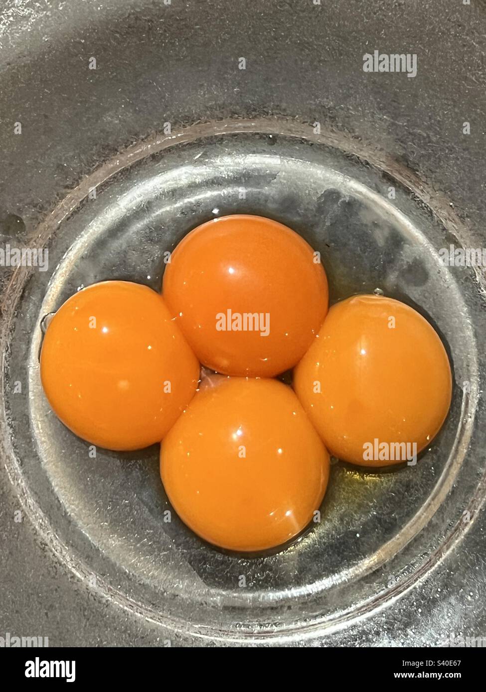 Four egg yolks in a glass mixing bowl to make custard Stock Photo Alamy