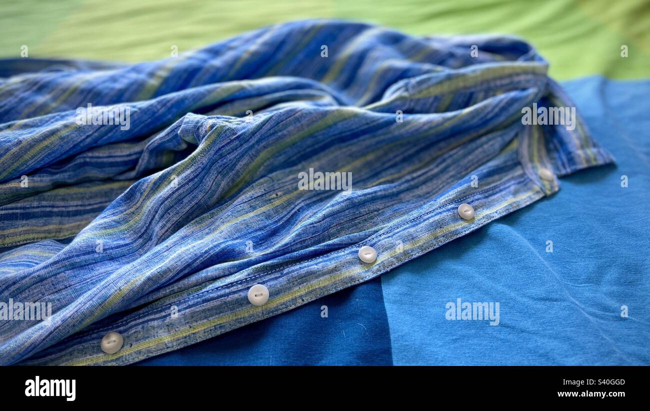 White buttons facing forward on blue, green and indigo linen shirt placed on a blue, green and indigo bed cover, creating abstract image, suitable for graphic background - Smartphone Captured Stock Image