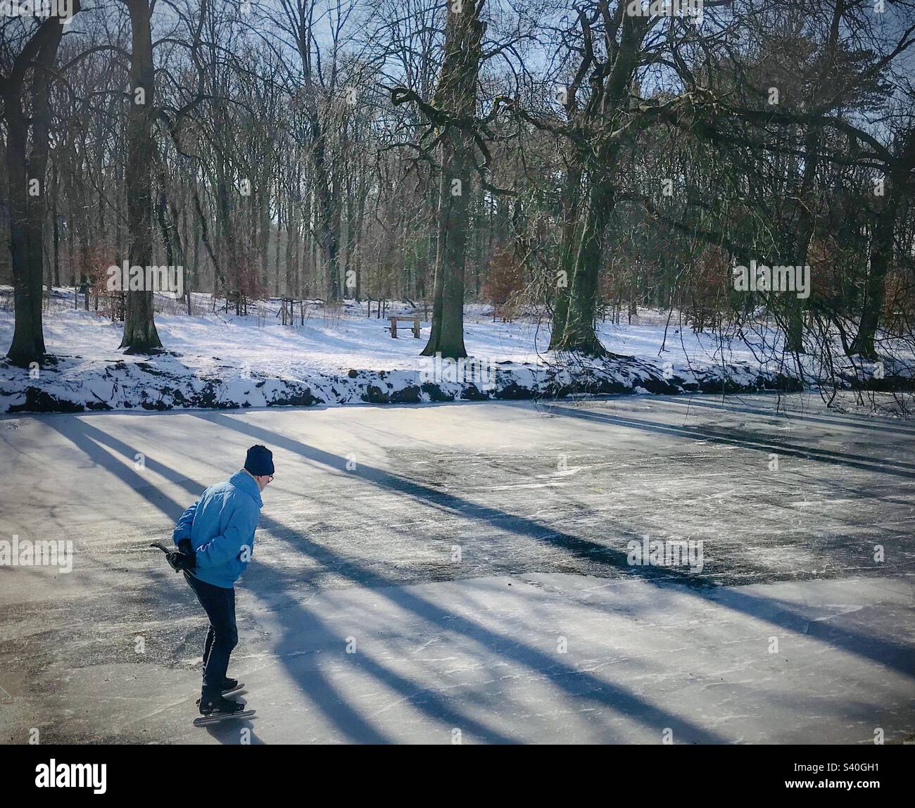 Old man on a blue coat ice-skating on a beautiful frozen outdoors lake - Smartphone Captured Stock Image