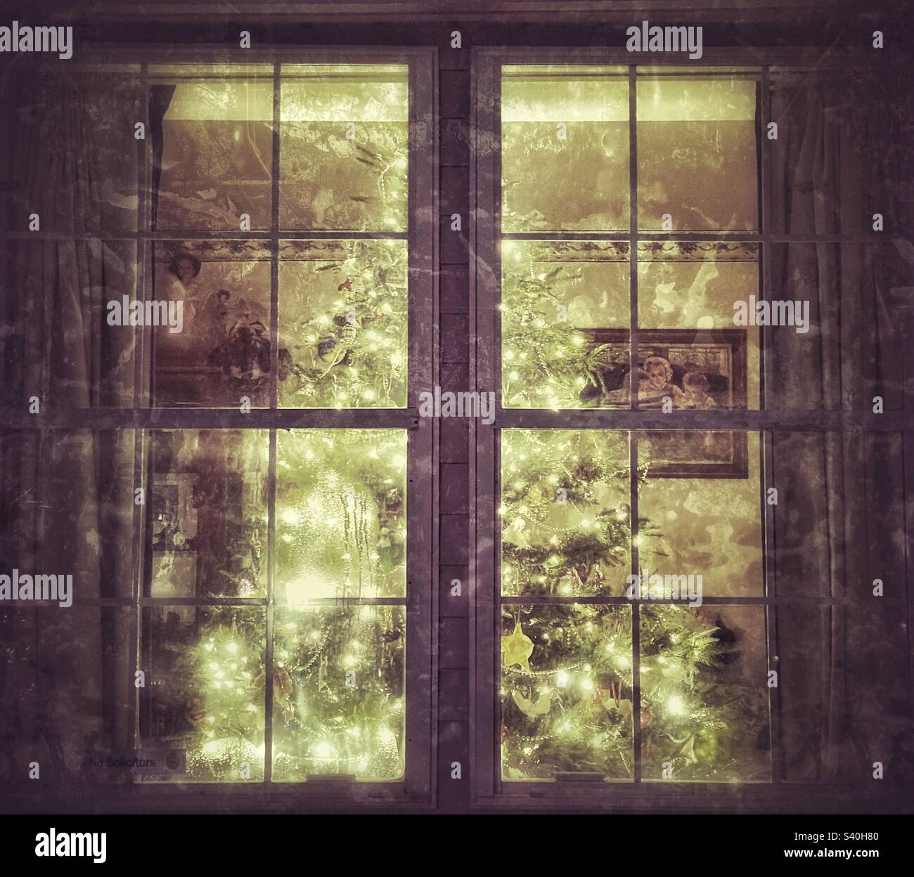 A beautiful artificial fir Christmas tree alighted with white lights as seen from the outside of this Utah home. IOS app Snapseed was used to give the image a vintage and grunge texture  and look. - Smartphone Captured Stock Image