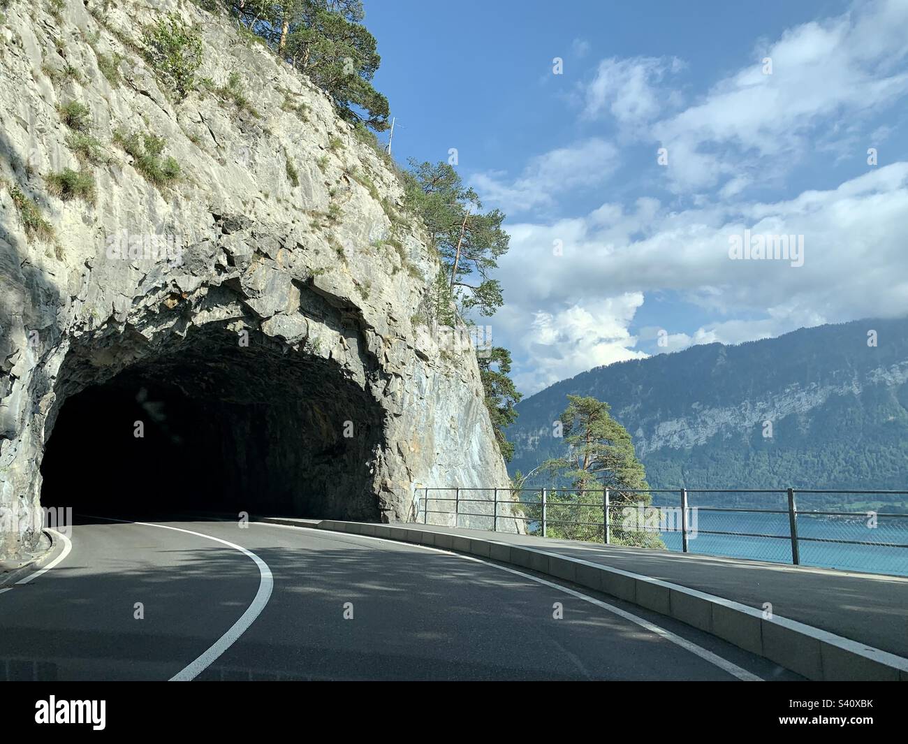 Road going into mountainside tunnel next to lake, Switzerland - Smartphone Captured Stock Image