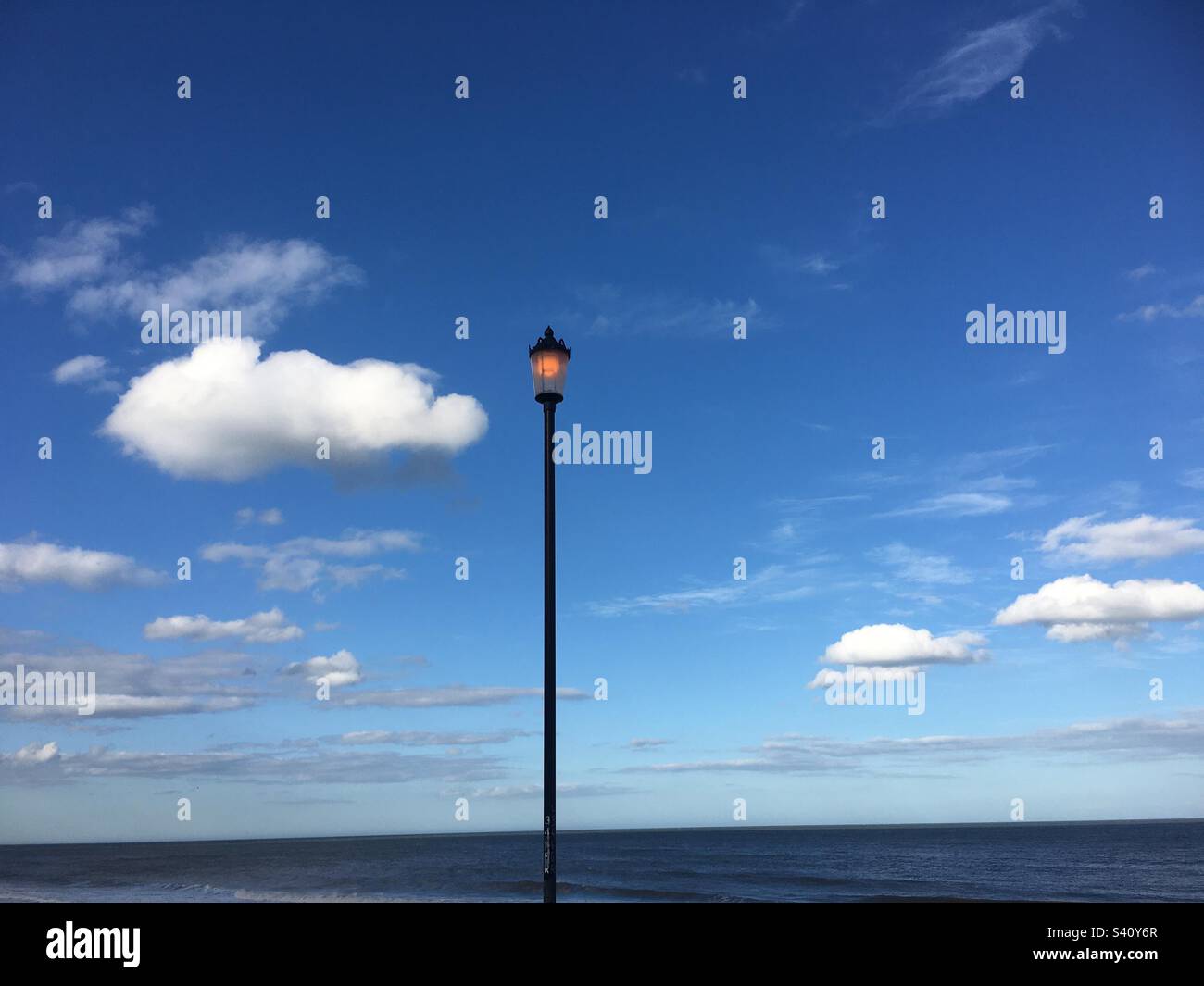 Blue sky with a lamppost, calm sea white clouds, Norfolk,UK - Smartphone Captured Stock Image