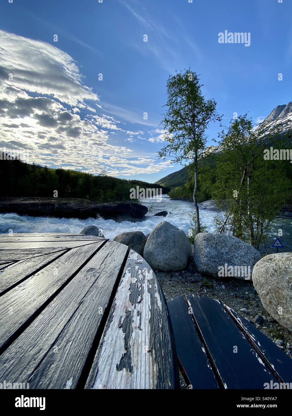 Sitting by the wooden table by the river for a lunch break, while having a road trip in Northern Norway - Smartphone Captured Stock Image