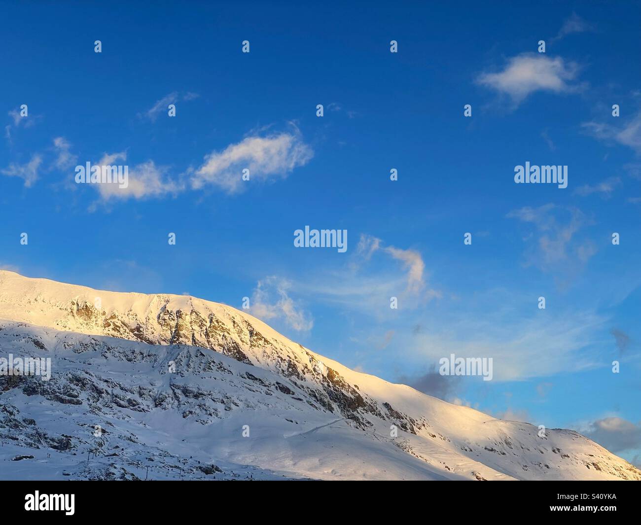 Wispy clouds in a blue sky over the snowy French Alps. Stock Photo