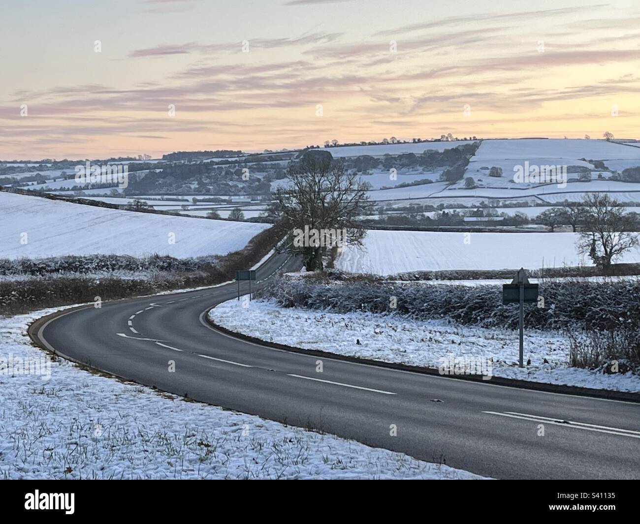 Clear road travelling through snow covered landscape as sun sets in the Cotswolds - Smartphone Captured Stock Image