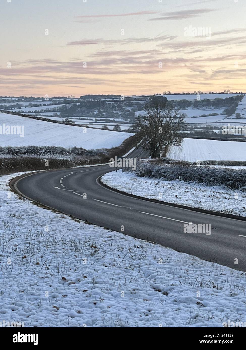 Clear road travelling through snow covered landscape as sun sets in the Cotswolds - Smartphone Captured Stock Image
