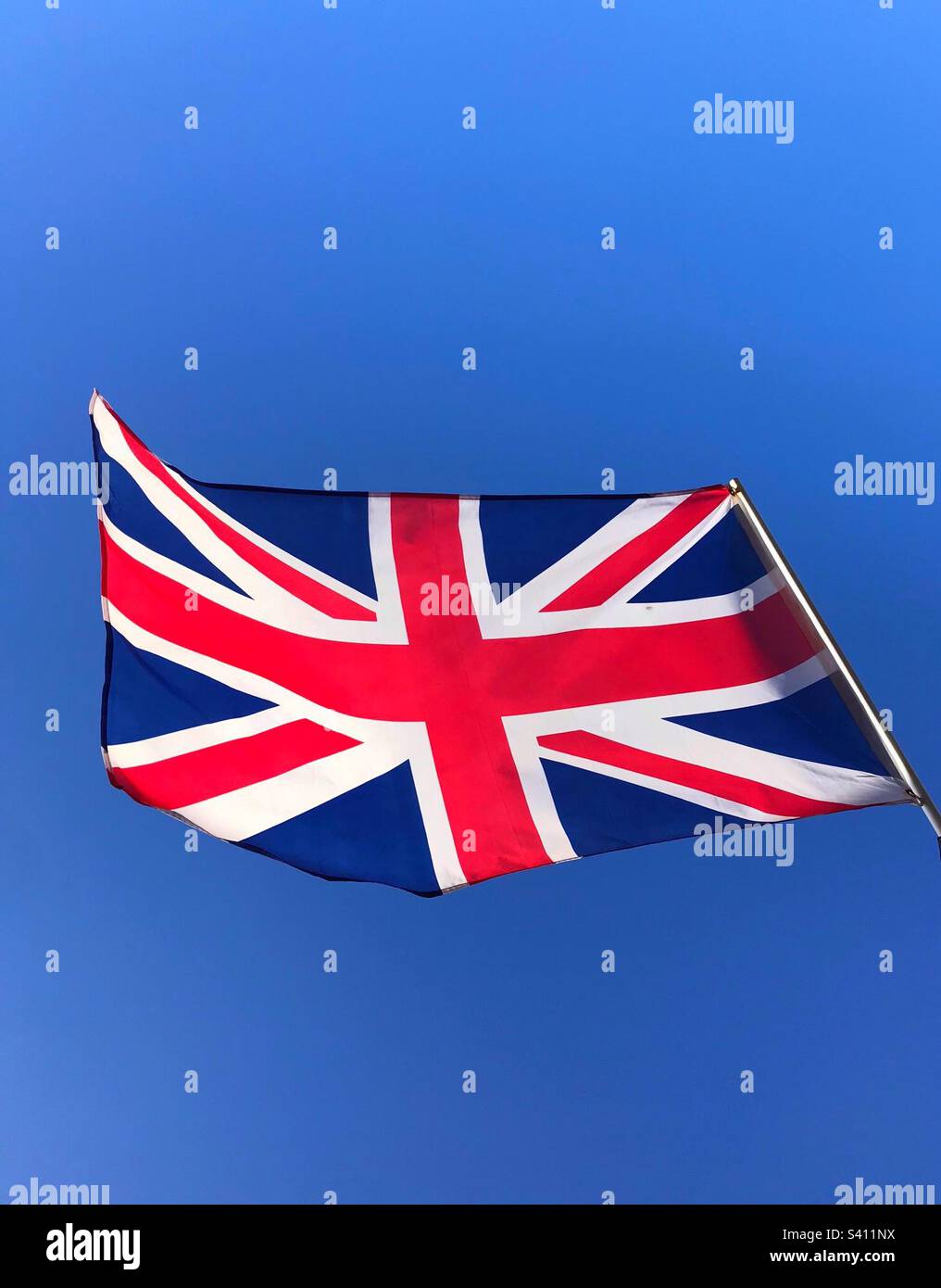 A Union Jack flying proudly against a bright blue sky - Smartphone Captured Stock Image