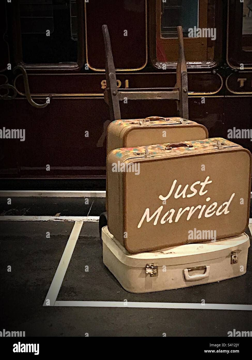 Vintage honeymoon suitcases on baggage cart on platform. National