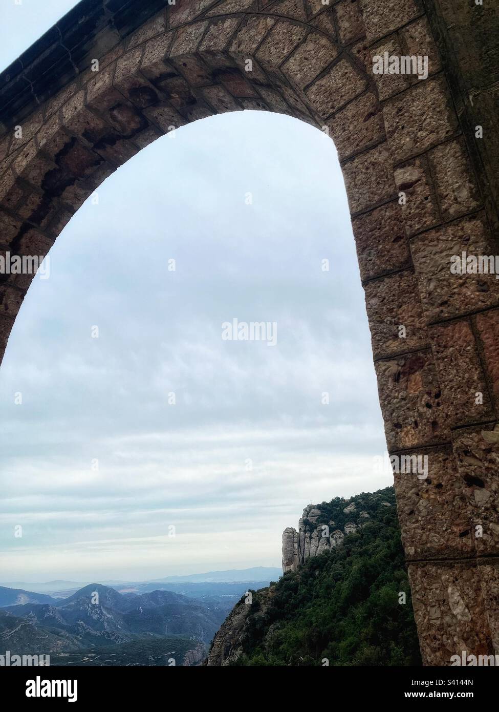 Looking through the arch on the outer wall of the Santa Maria de Montserrat Abbey in Spain’s Catalan lowlands. The Catholic Abbey is known for its choir and mountainous location - Smartphone Captured Stock Image