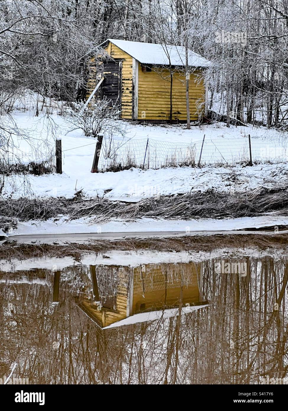 Little yellow hut shed on the river bank with reflection in the still water - Smartphone Captured Stock Image