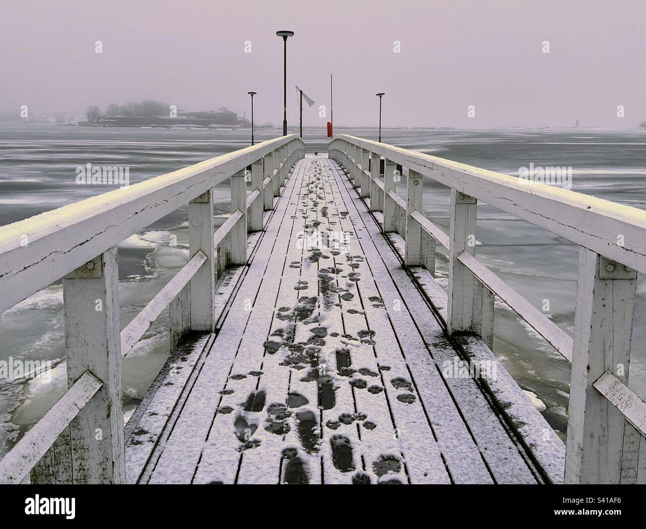 Wooden walking bridge with footprints in snow over water Baltic sea - Smartphone Captured Stock Image