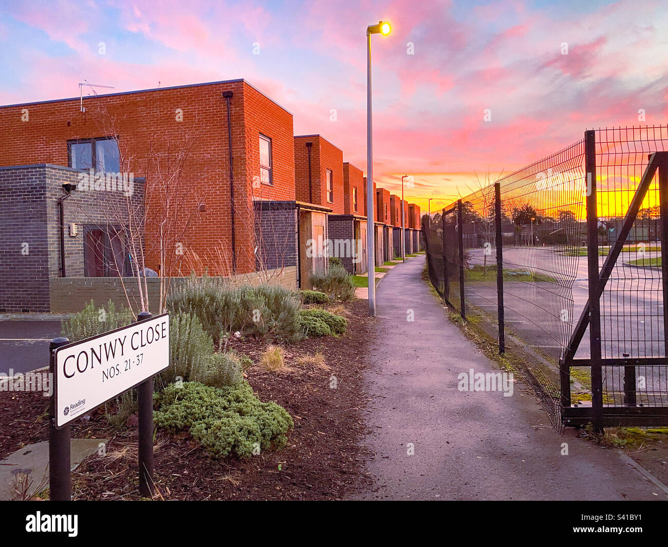 Walking down a pathway with town houses one side a d a fence on the other at sunset. - Smartphone Captured Stock Image