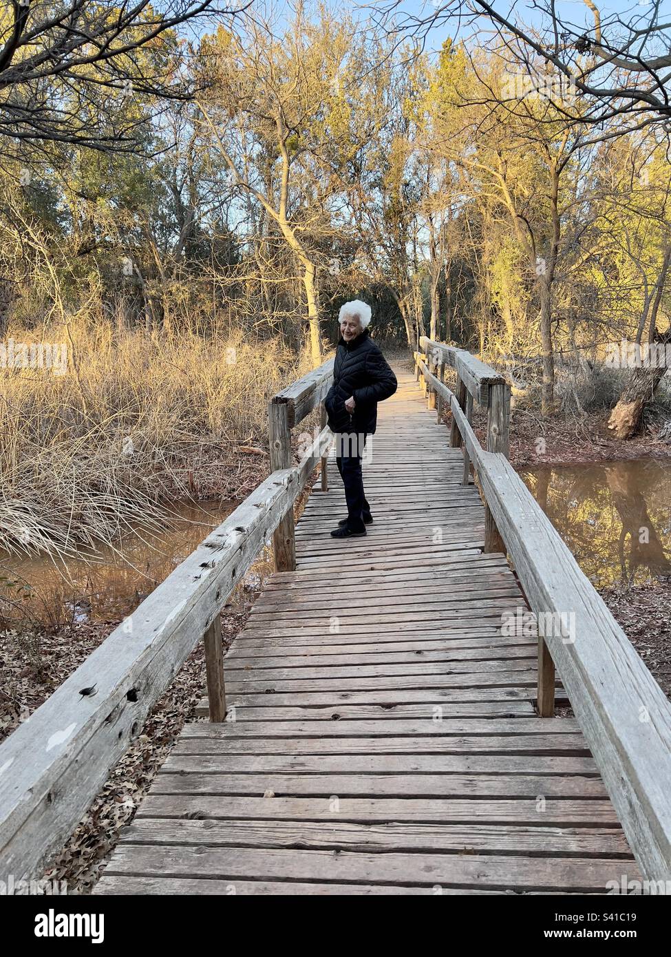 Beautiful silver haired active senior walking along a nature bridge and trail in Texas located in Abilene state park Stock Photo