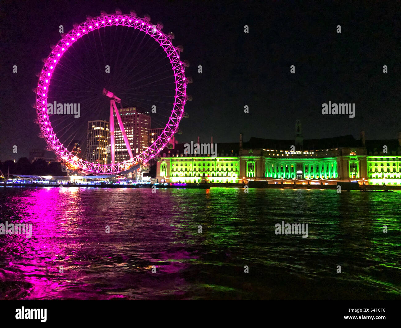 The London Eye at night illuminated in purple and County Hall in green