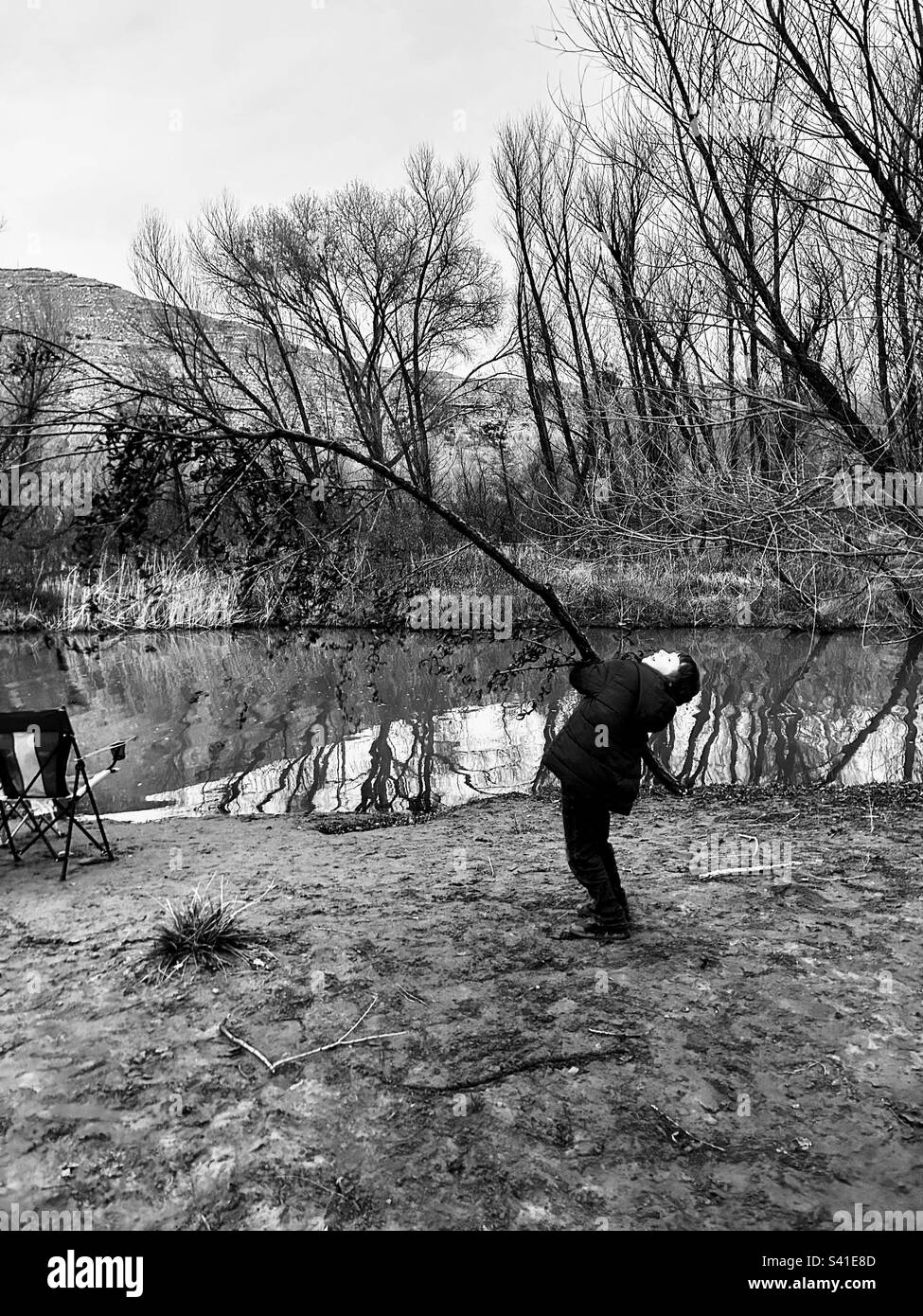 A boy using all of his strength to lift a branch bigger than him Stock