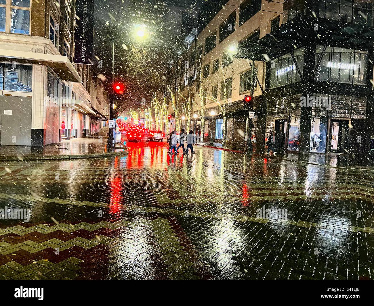 Night time snow falling in downtown Seattle, WA , USA with colourful red tail lights reflecting on wet brick streets in December. - Smartphone Captured Stock Image